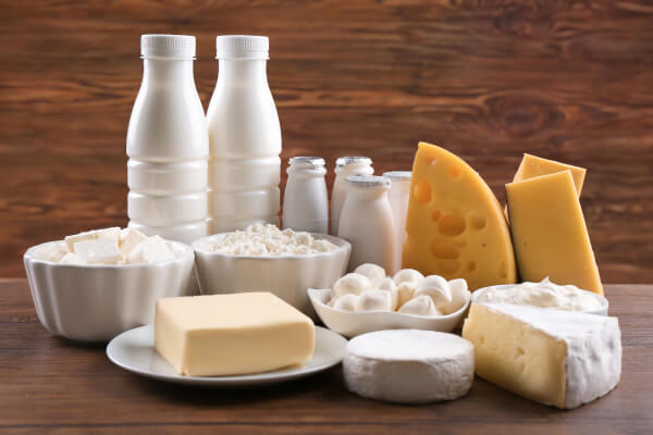 A variety of dairy products including milk bottles, butter, cheese wedges, and bowls of soft cheese on a wooden surface.